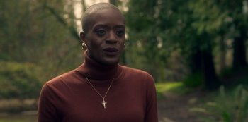 Movie still from “The Haunting of Bly Manor” (2020), directed by E.L. Katz – A woman in a brown sweater with a gold cross necklace; Close Up shot, Over the shoulder angle