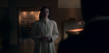 Movie still from “The Haunting of Bly Manor” (2020), directed by E.L. Katz – A woman in a white coat standing in a dark room; Medium shot, Over the shoulder angle