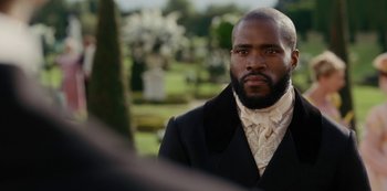 Movie still from “Bridgerton” (2020), created by Chris Van Dusen – A man wearing a suit and tie standing in front of a cemetery; Close Up shot, Over the shoulder angle