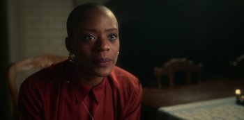 Movie still from “The Haunting of Bly Manor” (2020), directed by E.L. Katz – A woman in a red shirt sitting in front of a wooden table; Close Up shot, Over the shoulder angle