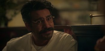 Movie still from “The Haunting of Bly Manor” (2020), directed by E.L. Katz – A man with a mustache and glasses sitting in a chair; Close Up shot, Over the shoulder angle