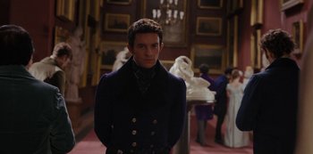 Movie still from “Bridgerton” (2020), created by Chris Van Dusen – A man standing in front of a group of people in a room; Medium shot, Over the shoulder angle