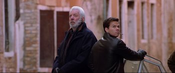 Movie still from “The Italian Job” (2003), directed by F. Gary Gray – A man and a man smoking a cigarette in front of a building; Medium shot, Low angle