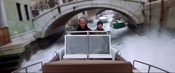 Movie still from “The Italian Job” (2003), directed by F. Gary Gray – Two men are riding a boat through a canal; Wide shot, High angle