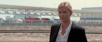 Movie still from “The Italian Job” (2003), directed by F. Gary Gray – A woman in a black jacket standing in front of train tracks; Medium shot, Low angle