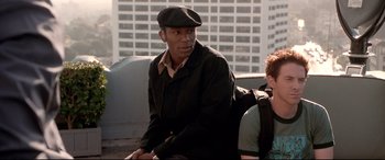 Movie still from “The Italian Job” (2003), directed by F. Gary Gray – A man sitting on top of a bus in front of a building; Medium shot, Over the shoulder angle