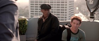 Movie still from “The Italian Job” (2003), directed by F. Gary Gray – A man sitting on top of a bench in front of a building; Medium shot, Over the shoulder angle
