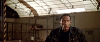 Movie still from “The Italian Job” (2003), directed by F. Gary Gray – A man standing in an industrial setting looking at the camera; Close Up shot, Low angle