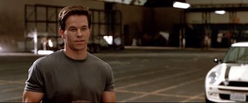 Movie still from “The Italian Job” (2003), directed by F. Gary Gray – A man standing in a parking lot wearing a gray shirt; Medium shot, Over the shoulder angle