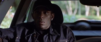 Movie still from “The Italian Job” (2003), directed by F. Gary Gray – A man wearing a hat and ear buds sitting in a car; Close Up shot, High angle