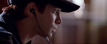 Movie still from “The Italian Job” (2003), directed by F. Gary Gray – A young man wearing a hat and ear buds; Close Up shot, Over the shoulder angle
