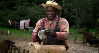 Movie still from “The Jerk” (1979), directed by Carl Reiner – A man wearing a straw hat and overalls is cutting paper; Medium shot, Low angle