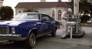 Movie still from “The Jerk” (1979), directed by Carl Reiner – A man standing in front of a blue car; Wide shot, Low angle