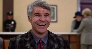 Movie still from “The Jerk” (1979), directed by Carl Reiner – A man in a suit and tie smiling for the camera; Close Up shot, Over the shoulder angle