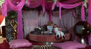 Movie still from “The Jerk” (1979), directed by Carl Reiner – Two young children sitting on a bed in a pink room; Wide shot, High angle