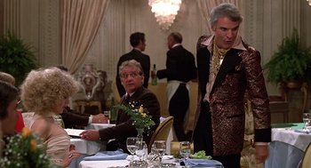 Movie still from “The Jerk” (1979), directed by Carl Reiner – A man in a suit standing at a table with other people; Medium shot, Over the shoulder angle