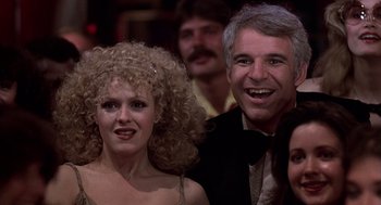 Movie still from “The Jerk” (1979), directed by Carl Reiner – A man and a woman posing for a picture in front of a crowd; Close Up shot, Over the shoulder angle