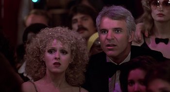 Movie still from “The Jerk” (1979), directed by Carl Reiner – A man and a woman are standing in front of a group of people; Close Up shot, Low angle
