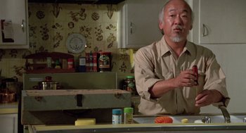 Movie still from “The Karate Kid” (1984), directed by John G. Avildsen – An older man standing in front of a kitchen counter; Medium shot, Low angle