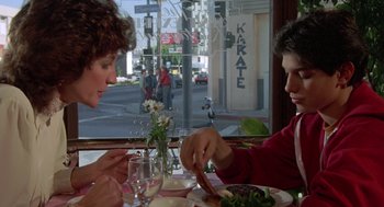 Movie still from “The Karate Kid” (1984), directed by John G. Avildsen – A man and a woman sitting at a table with food; Medium shot, Over the shoulder angle