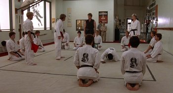 Movie still from “The Karate Kid” (1984), directed by John G. Avildsen – A group of people in a room practicing martial arts; Wide shot, Over the shoulder angle
