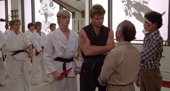 Movie still from “The Karate Kid” (1984), directed by John G. Avildsen – A group of men standing next to each other in a room; Medium shot, Over the shoulder angle