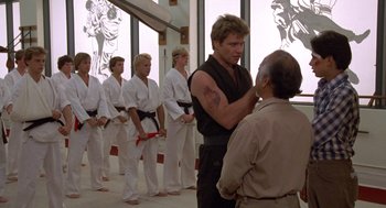 Movie still from “The Karate Kid” (1984), directed by John G. Avildsen – A group of men standing next to each other in a room; Medium shot, Over the shoulder angle