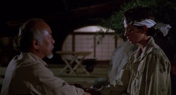 Movie still from “The Karate Kid” (1984), directed by John G. Avildsen – Two men shaking hands in front of an outdoor setting; Medium shot, Over the shoulder angle