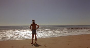 Movie still from “The Karate Kid” (1984), directed by John G. Avildsen – A man standing on the beach looking out at the ocean; Wide shot, Low angle