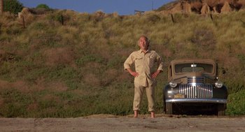 Movie still from “The Karate Kid” (1984), directed by John G. Avildsen – A man standing in front of a car on the side of the road; Wide shot, Low angle