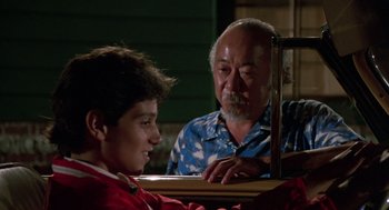 Movie still from “The Karate Kid” (1984), directed by John G. Avildsen – An older man and a young boy looking at each other in front of a mirror; Medium shot, Over the shoulder angle