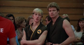 Movie still from “The Karate Kid” (1984), directed by John G. Avildsen – Two young men standing next to each other in front of a group of people; Close Up shot, Low angle