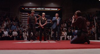 Movie still from “The Karate Kid” (1984), directed by John G. Avildsen – A group of men standing on a stage in front of an audience; Wide shot, Over the shoulder angle
