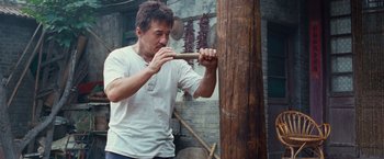 Movie still from “The Karate Kid” (2010), directed by Harald Zwart – A man holding an axe in front of a wooden pole; Medium shot, Low angle
