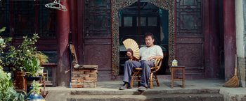 Movie still from “The Karate Kid” (2010), directed by Harald Zwart – A man sitting in a chair holding a fan; Wide shot, Low angle