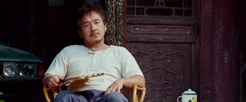 Movie still from “The Karate Kid” (2010), directed by Harald Zwart – A man sitting in a chair holding a guitar in his hand; Medium shot, Low angle