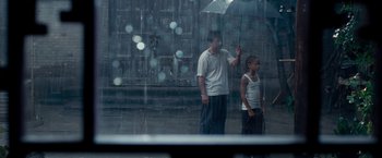 Movie still from “The Karate Kid” (2010), directed by Harald Zwart – A man holding an umbrella over a child; Wide shot, Over the shoulder angle