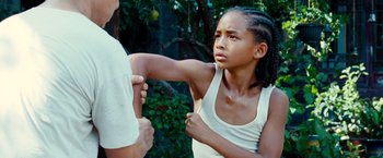 Movie still from “The Karate Kid” (2010), directed by Harald Zwart – A young girl holding a man's arm in front of a tree; Medium shot, Low angle