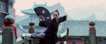 Movie still from “The Karate Kid” (2010), directed by Harald Zwart – A man holding an umbrella while standing on one leg; Medium shot, Low angle