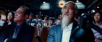 Movie still from “The Karate Kid” (2010), directed by Harald Zwart – An old man with long white beard sitting in front of a group of people; Close Up shot, Low angle