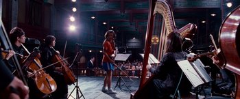 Movie still from “The Karate Kid” (2010), directed by Harald Zwart – A woman standing in front of an audience holding a harp; Wide shot, Low angle