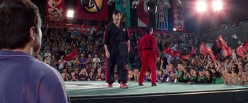 Movie still from “The Karate Kid” (2010), directed by Harald Zwart – Two men in red and black outfits on a stage; Wide shot, Low angle