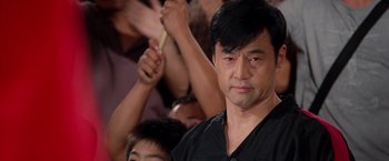 Movie still from “The Karate Kid” (2010), directed by Harald Zwart – A person holding a stick in a crowd; Close Up shot, Over the shoulder angle