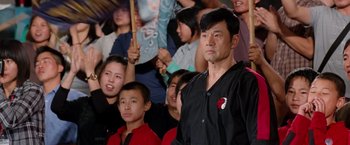 Movie still from “The Karate Kid” (2010), directed by Harald Zwart – A group of people sitting in front of a crowd of people; Medium shot, Over the shoulder angle