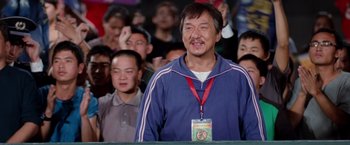 Movie still from “The Karate Kid” (2010), directed by Harald Zwart – A man with a badge around his neck is standing in front of a group of people; Medium shot, Low angle