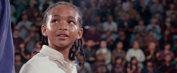 Movie still from “The Karate Kid” (2010), directed by Harald Zwart – A young girl with braids looking up in front of a crowd of onlookers; Close Up shot, Low angle