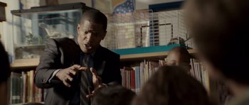 Movie still from “The Kingdom” (2007), directed by Peter Berg – A man in a suit and tie talking to a crowd; Medium shot, Over the shoulder angle