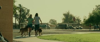 Movie still from “The Kingdom” (2007), directed by Peter Berg – A man and a woman walking a dog down a sidewalk; Wide shot, Low angle