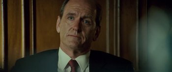 Movie still from “The Kingdom” (2007), directed by Peter Berg – An older man in a suit and tie looking at the camera; Close Up shot, Low angle