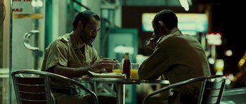 Movie still from “The Kingdom” (2007), directed by Peter Berg – Two men are sitting at a table and one of them is holding a cell phone up to his ear; Medium shot, Over the shoulder angle